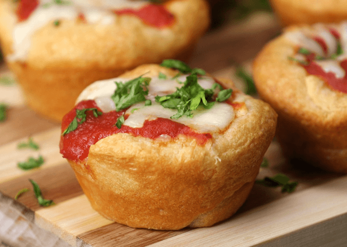 Mini PIzza Muffins with shredded cheese, tomato sauce, and fresh herbs