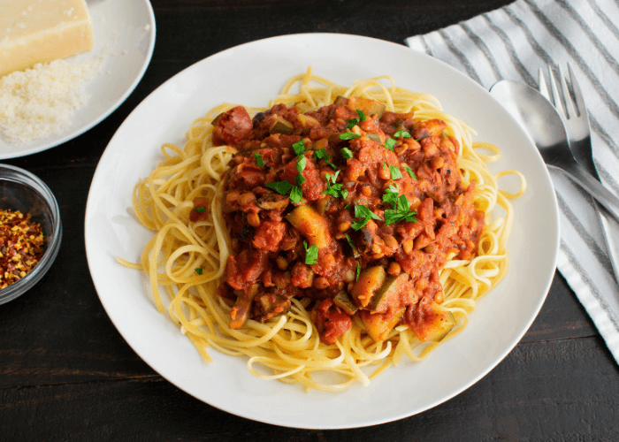 Red lentil bolognese on top of spaghetti noodles on a white plate.