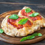 Mini calzones on a cutting board with pizza sauce and basil leaves