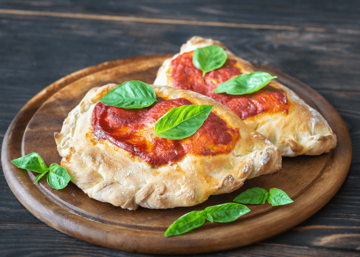 Mini calzones on a cutting board with pizza sauce and basil leaves