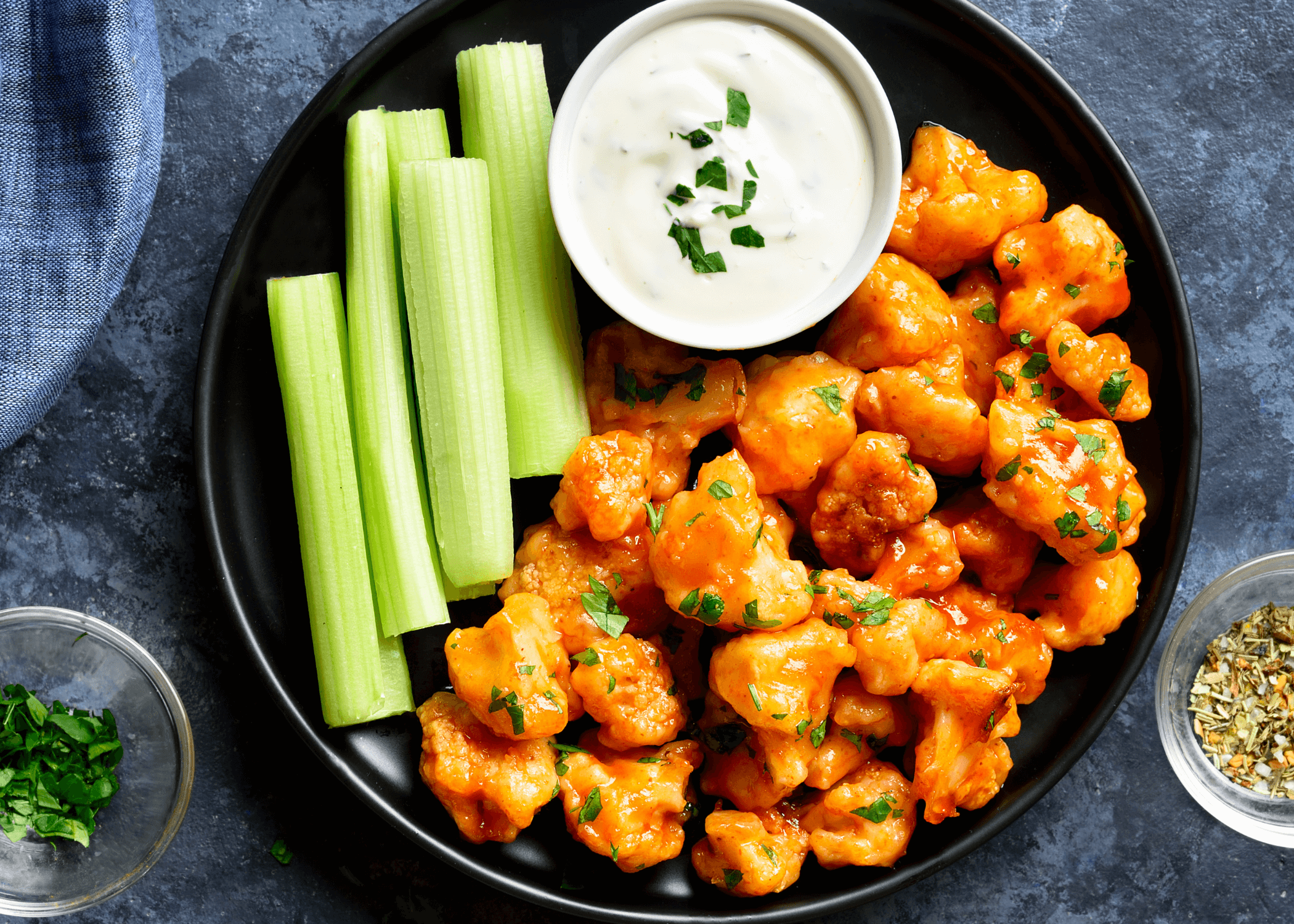 Buffalo Roasted Cauliflower on a black plate with ranch and celery sticks