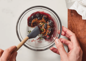 Hands mixing blueberry jam, mustard, and rosemary