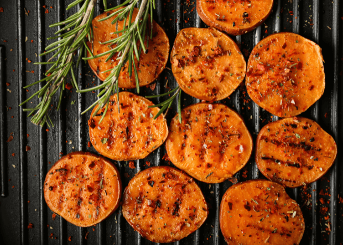 Sliced sweet potatoes on the grill with rosemary
