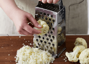 Person using a cauliflower floret on a box grater