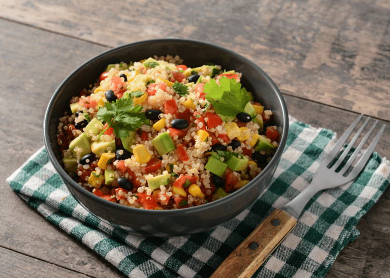 Mexican Quinoa with avocados, corn, tomatoes in a black bowl with checkered hand towel