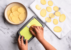 Sliced potatoes on a plate and a slicer cutting the potato