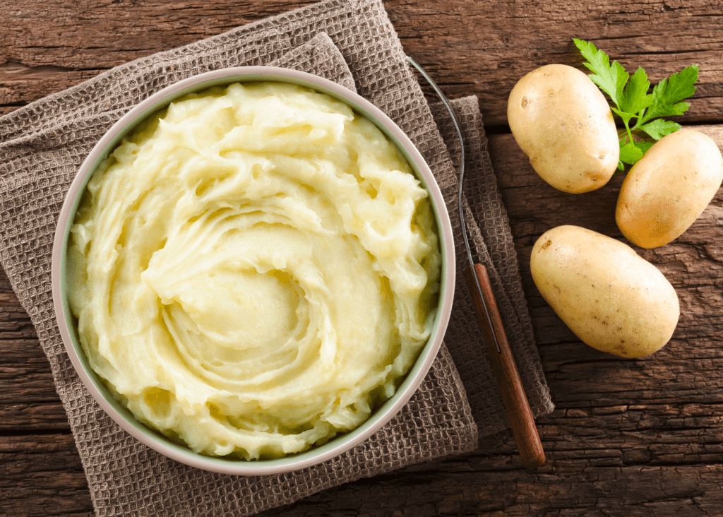 mashed potatoes in a bowl with two russet potatoes on the table