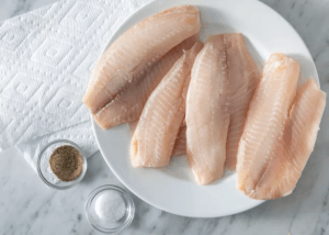 tilapia fillets on a white plate with two bowls of seasonings