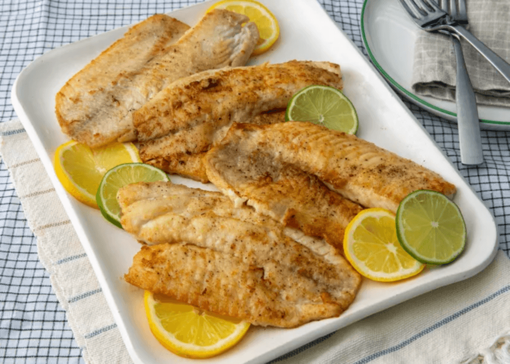 Pan-Seared Tilapia fillets, lemons, and limes on a white plate